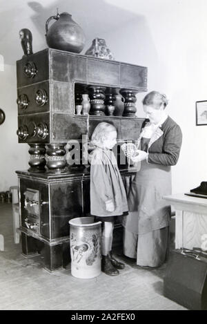 Eine aus dem Töpfermeisterin Kannenbäckerland zeigt einen einem kleinen Mädchen fertig gebrannten Tonkrug, 1930er Jahre Deutschland. Un maître potter est montrant une cruche en grès fin à une petite fille, Allemagne 1930. Banque D'Images