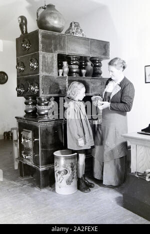 Eine aus dem Töpfermeisterin Kannenbäckerland zeigt einen einem kleinen Mädchen fertig gebrannten Tonkrug, 1930er Jahre Deutschland. Un maître potter est montrant une cruche en grès fin à une petite fille, Allemagne 1930. Banque D'Images