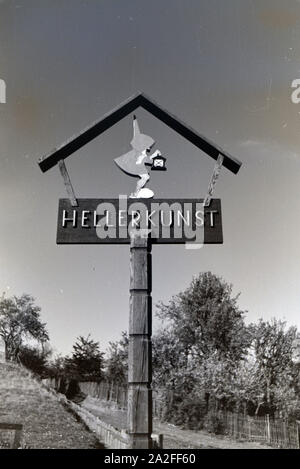 Eingangsschild das zu den Heller Kunst Werkstätten in der Eifel mit dem Märchenmotiv Zwerges und mit Laterne, Deutschland 1930 er Jahre. La plaque signalétique de l'Heller Kunst des ateliers dans l'Eifel avec le motif de conte d'un nain avec une lanterne, Allemagne 1930. Banque D'Images