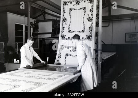 Zwei Mitarbeiter einer Textilfirma Stofbahn à Krefeld bedrucken eine mit einem Blumenmuster durch das Siebdruckverfahren, Deutschland 1930 er Jahre. Deux employés d'une entreprise textile à Krefeld sérigraphie d'un motif floral sur un panneau, l'Allemagne des années 1930. Banque D'Images