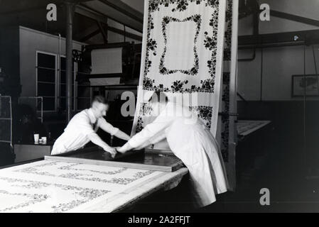 Zwei Mitarbeiter einer Textilfirma Stofbahn à Krefeld bedrucken eine mit einem Blumenmuster durch das Siebdruckverfahren, Deutschland 1930 er Jahre. Deux employés d'une entreprise textile à Krefeld sérigraphie d'un motif floral sur un panneau, l'Allemagne des années 1930. Banque D'Images