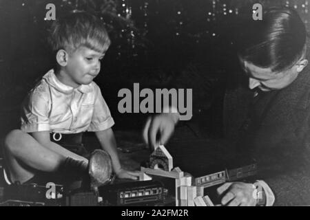 Typisches Weihnachtsbild : Der kleine Sohn bekommt eine Eisenbahn geschenkt Vater und der damit, Deutschland Spielt er Jahre années 1930. typique de noël photo : un petit garçon est un petit train et son père joue avec elle, l'Allemagne des années 1930. Banque D'Images