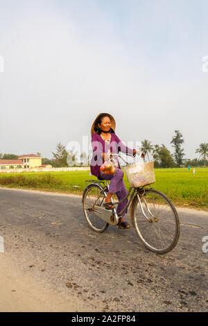 Hoi An, Vietnam - 3 mars 2010 : femme de rouler à vélo à travers les rizières. Le vélo est encore une forme populaire de transport. Banque D'Images