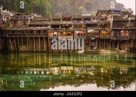 Hunan, Chine, 14 Novembre 2011 : les vieilles maisons en équilibre sur des pilotis de bois le long de la rivière. Banque D'Images