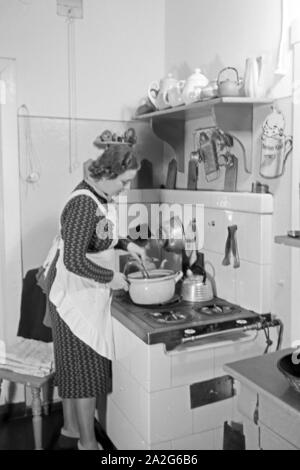 Eine Frau steht am herd in der Küche und kocht, Deutschland 1930 er Jahre. Une femme debout dans la cuisine sur la cuisson au four, l'Allemagne des années 1930. Banque D'Images