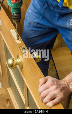 Carpenter fait un trou dans la porte en bois ancien pour boitier de serrure à l'aide d'une perceuse. Close-up. Banque D'Images