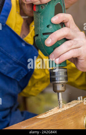 Carpenter fait un trou dans la porte en bois ancien pour boitier de serrure à l'aide d'une perceuse. Close-up. Banque D'Images