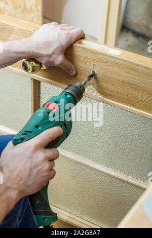 Carpenter fait un trou dans la porte en bois ancien pour boitier de serrure à l'aide d'une perceuse. Close-up. Banque D'Images