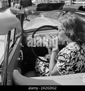 Eine junge Frau raucht am Steuer von Opel Olympia, Deuitschland 1930er Jahre. Un ypung femme fumant dans son modèle Opel Olympia, Allemagne 1930. Banque D'Images