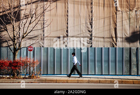 Homme d'affaires japonais marcher sur un trottoir à côté de chantier en cas de forte lumière du soleil d'hiver Banque D'Images