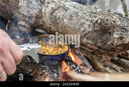L'homme prépare un repas sur un feu de camp tout en maintenant un métal au-dessus du feu. Close-up. Banque D'Images