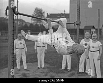 Ein Turner aus der Altherrenriege Turnvereins trägt und eine Übung suis vor Reck, Deutschland 1930er Jahre. Un membre de la haute direction du ministère d'un gymnastic club d'effectuer à un bar sur un terrain de sport, de l'Allemagne des années 1930. Banque D'Images