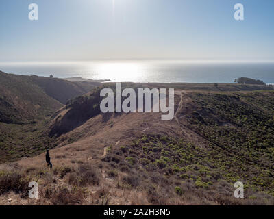 Garçon marche sur sentier sur une falaise donnant sur l'océan Pacifique mousseux aux beaux jours, la lumière du soleil reflétant sur l'océan, parc d'État de Montana de Oro, Los Osos, Ca Banque D'Images