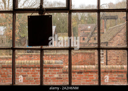 Voir d'une scène industrielle victorienne à travers une fenêtre en fonte avec vitres sales et une tenture blank sign Banque D'Images