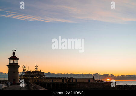 Le lever du soleil sur la mer, la manche de Ramsgate Harbour et le phare sur la côte du Kent. Lever de soleil sur la mer directement dans une fine couche de brouillard à l'horizon avec un ciel nuageux au-dessus de cela. Ciel change de l'orange, jaune à bleu avec quelques nuages vaporeux. Banque D'Images