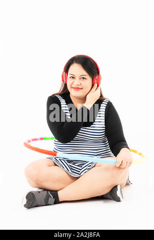 Grosse femme se reposer et écouter de la musique de casque rouge après l'exercice par Hula-Hoop colorés. Elle sourit et aime perdre du poids pour son bette Banque D'Images