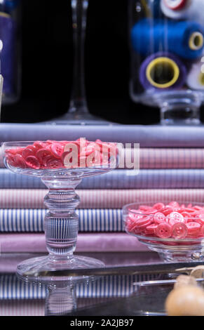 Ciseaux de tailleur, poinçon, craie et virole présenté sur table en verre, entouré par des boutons et tissu chemise Banque D'Images