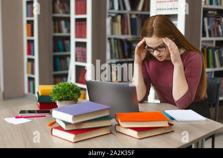 Fatigué redhead girl sitting in front of laptop, serrant head Banque D'Images