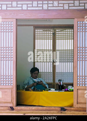 SEPT. 19, 2019 Séoul CORÉE DU SUD-Coréen : gentleman regarder à partir de son téléphone mobile et assis à l'intérieur d'une maison traditionnelle coréenne Banque D'Images