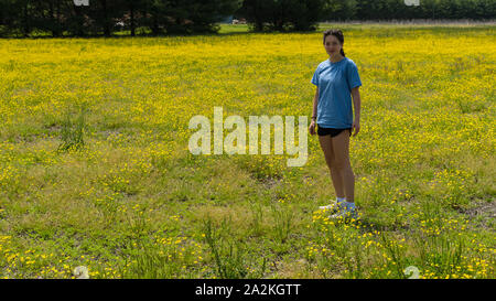 Teen girl in shorts debout dans un grand champ avec des fleurs jaunes et des arbres en arrière-plan Banque D'Images