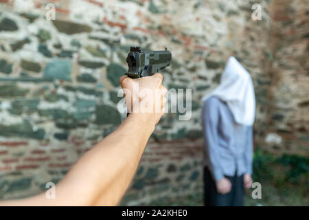 Une main avec un pistolet marque un homme avec une capuche sur sa tête. selective focus Banque D'Images