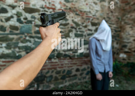 Une main avec un pistolet marque un homme avec une capuche sur sa tête. selective focus Banque D'Images