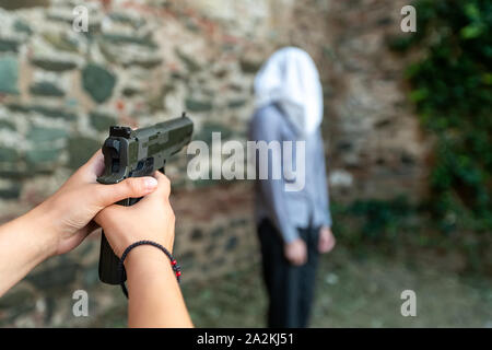 Une main avec un pistolet marque un homme avec une capuche sur sa tête. selective focus Banque D'Images