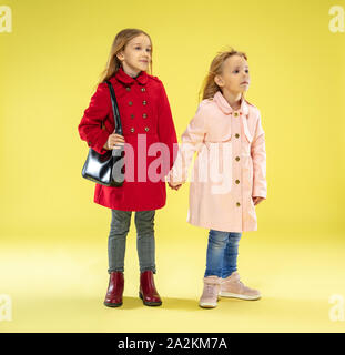 Un portrait d'un brillant portrait à la mode in un imperméable tenant un sac noir sur fond jaune studio. L'automne et au printemps, à la mode pour enfants. Cute blonde élégant. Banque D'Images