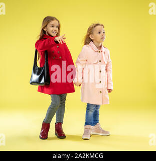 Un portrait d'un brillant portrait à la mode in un imperméable tenant un sac noir sur fond jaune studio. L'automne et au printemps, à la mode pour enfants. Cute blonde élégant. Banque D'Images