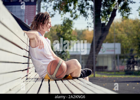 Photo de l'homme sportif avec volley-ball ball assis sur banc en bois sur la journée d'été Banque D'Images