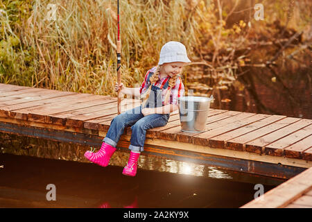 Une petite fille avec une canne à pêche ressemble à la prise de poissons dans un seau. Banque D'Images