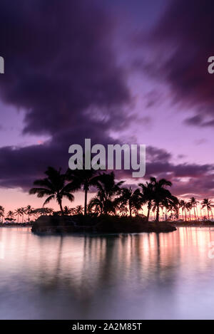 Coucher de soleil sur une plage hawaïenne. Le ciel est violet, rouge et orange, comme le soleil plonge derrière la silhouette des palmiers, sur Oahu, Hawaii Banque D'Images