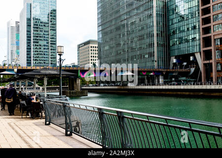 Les visiteurs prendre des rafraîchissements dans un café donnant sur la voie d'eau à Canary Wharf avec chemin de fer et les édifices en arrière-plan., Banque D'Images