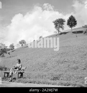 Eine junge Frau sitzt auf einer Bank im Schwarzwald, Deutschland 1930er Jahre. Une jeune femme assise sur un banc dans la région de la Forêt-Noire, Allemagne 1930. Banque D'Images