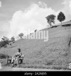 Eine junge Frau sitzt auf einer Bank im Schwarzwald, Deutschland 1930er Jahre. Une jeune femme assise sur un banc dans la région de la Forêt-Noire, Allemagne 1930. Banque D'Images