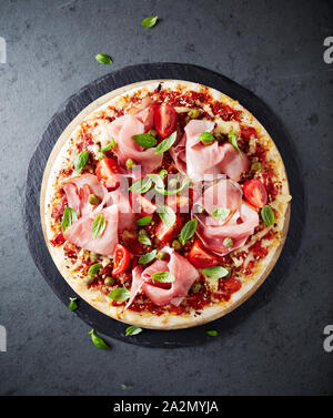 Pizza garnie de jambon forêt noire, câpres, tomates cerises et basilic frais. Pizza italienne. La nourriture faite maison. Banque D'Images