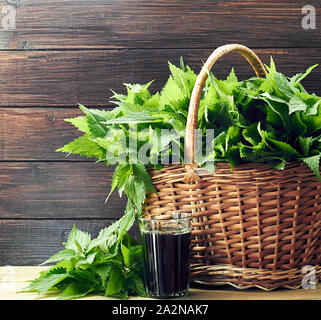 Jus d'ortie ou décoction dans un verre à proximité de l'osier de fines herbes fraîches, des plantes sur une table en bois sur fond rustique, Urtica dioica est un polyvitaminic dieta Banque D'Images