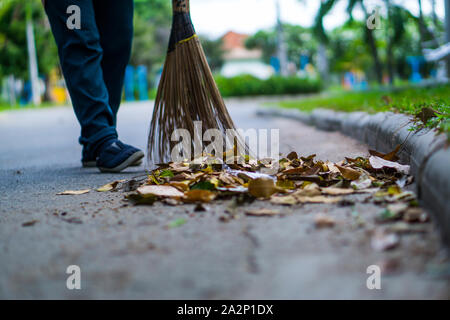 Une femme asiatique qui balayent les feuilles sèches par la route dans le jardin extérieur. Concept de nettoyage. Banque D'Images