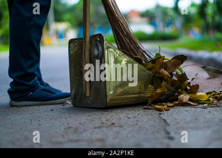 Une femme asiatique qui balayent les feuilles sèches par la route dans le jardin extérieur. Concept de nettoyage. Banque D'Images