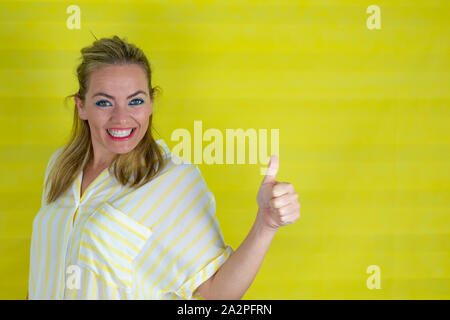 Jeune femme blonde sur fond isolé avec sourire heureux face à la recherche et en pointant avec thumb up - Image Banque D'Images