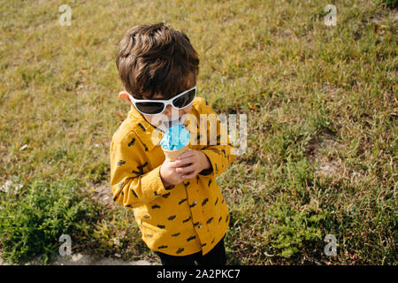 Jeune garçon portant des lunettes de soleil et la consommation de crème glacée sur une journée ensoleillée Banque D'Images