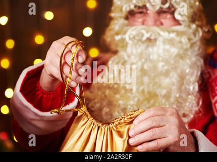Le Père Noël ouvre un sac de cadeaux, assis près de l'arbre de Noël décoré avec des lumières - Joyeux Noël et bonnes fêtes ! Banque D'Images