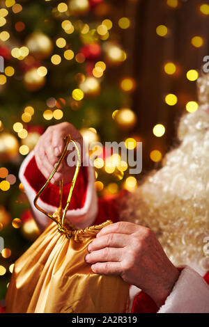 Le Père Noël ouvre un sac de cadeaux, assis près de l'arbre de Noël décoré avec des lumières - Joyeux Noël et bonnes fêtes ! Banque D'Images