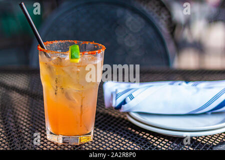 Un cocktail de couleur orange est assis sur une table en métal à côté de quelques verres et couverts, roulée dans de serviettes en tissu. Banque D'Images