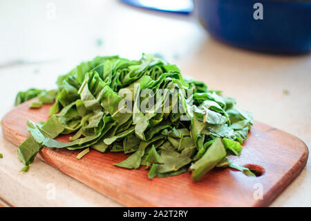 Les jeunes tranches d'oseille verte pour le borscht et salade se trouve sur une planche à découper, de style rustique, le matin dans la lumière du soleil. Copier l'espace. Banque D'Images