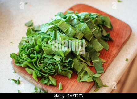 Les jeunes tranches d'oseille verte pour le borscht et salade se trouve sur une planche à découper, de style rustique, le matin dans la lumière du soleil. Copier l'espace. Banque D'Images