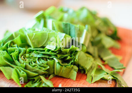 Les jeunes tranches d'oseille verte pour le borscht et salade se trouve sur une planche à découper, de style rustique, le matin dans la lumière du soleil. Copier l'espace. Banque D'Images