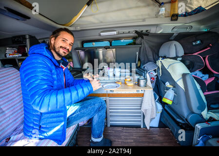 Ce qui fait du petit déjeuner ou déjeuner dans un camping-car, camping-car ou camping. Les jeunes dans la préparation des aliments guy Hippie Camper van lors d'un déplacement avec RV, autocaravane caravane ou Banque D'Images