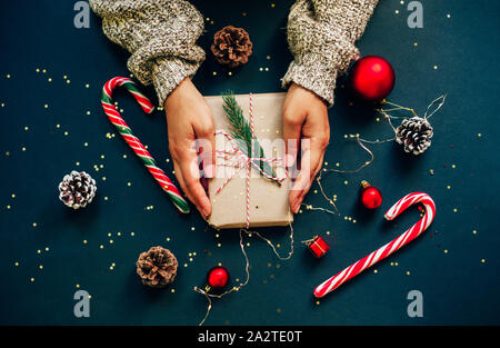 Artisanat de Noël boîte-cadeau avec des rubans rouges, des pommes de pin et des décorations d'or et rouge contre fond bleu foncé. Don de femmes. Banque D'Images