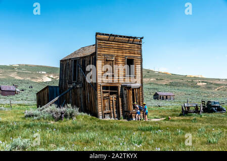 Deux visiteurs d'oeil dans une fenêtre de la structure de l'hôtel Swazey encore debout, s'inclinent, à Bodie State Historic Park et ville fantôme. Banque D'Images